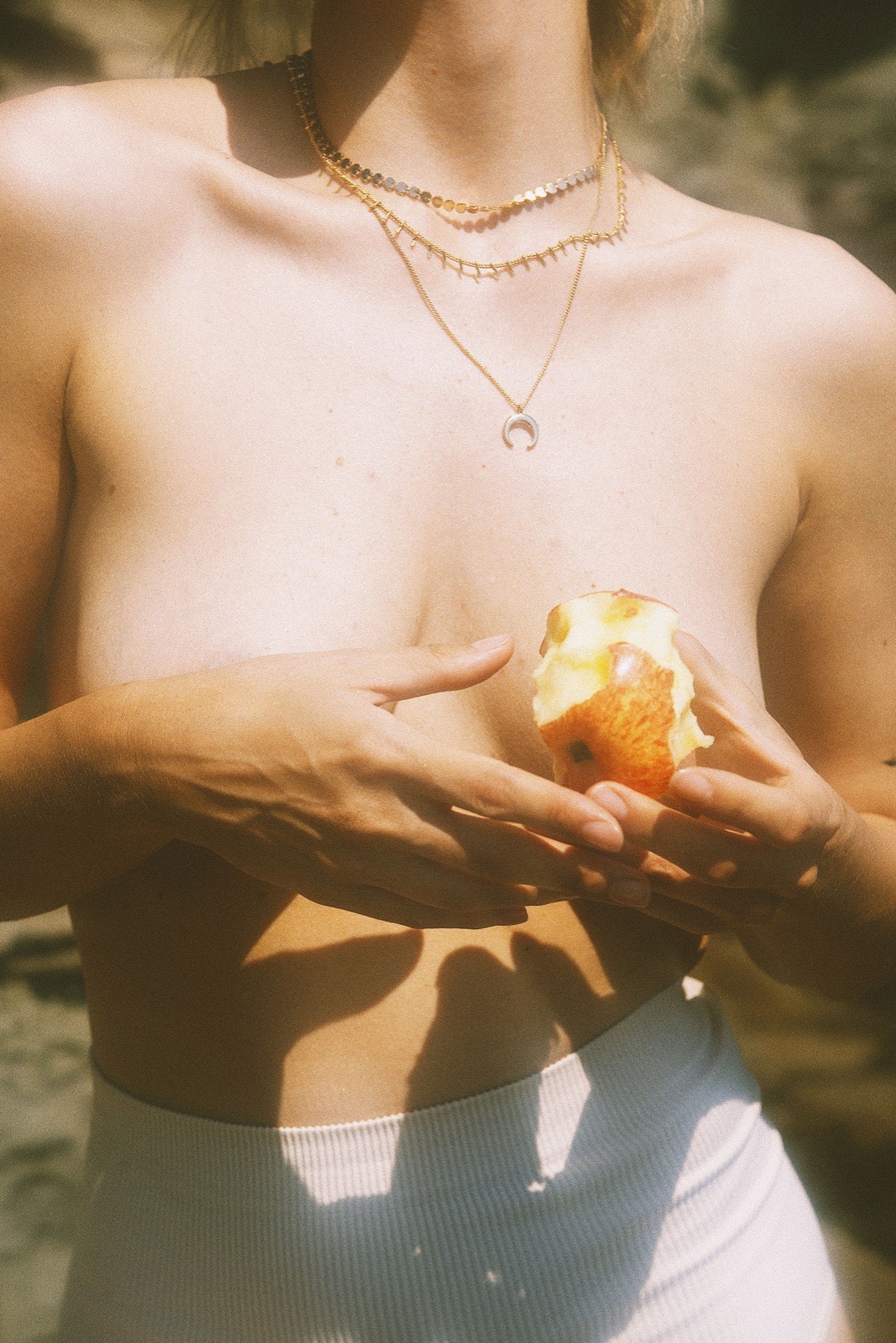 A woman holding a bitten apple in front of her chest